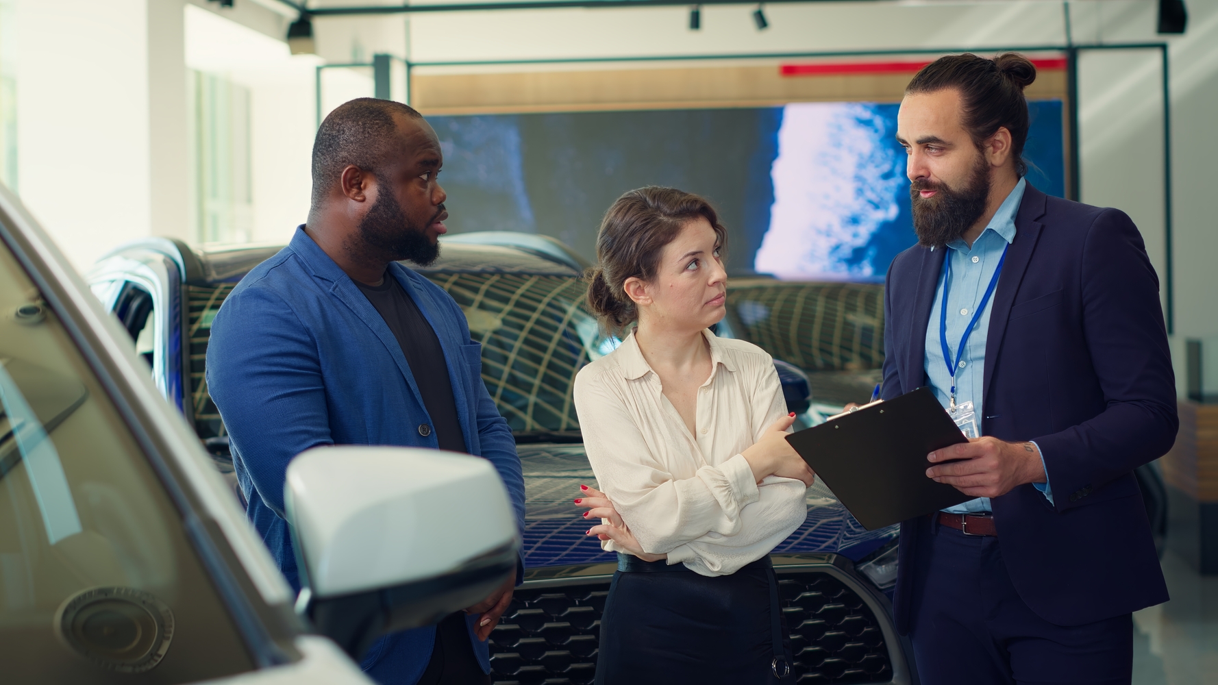 Car dealership salesman reading clipboard to customers, providing information