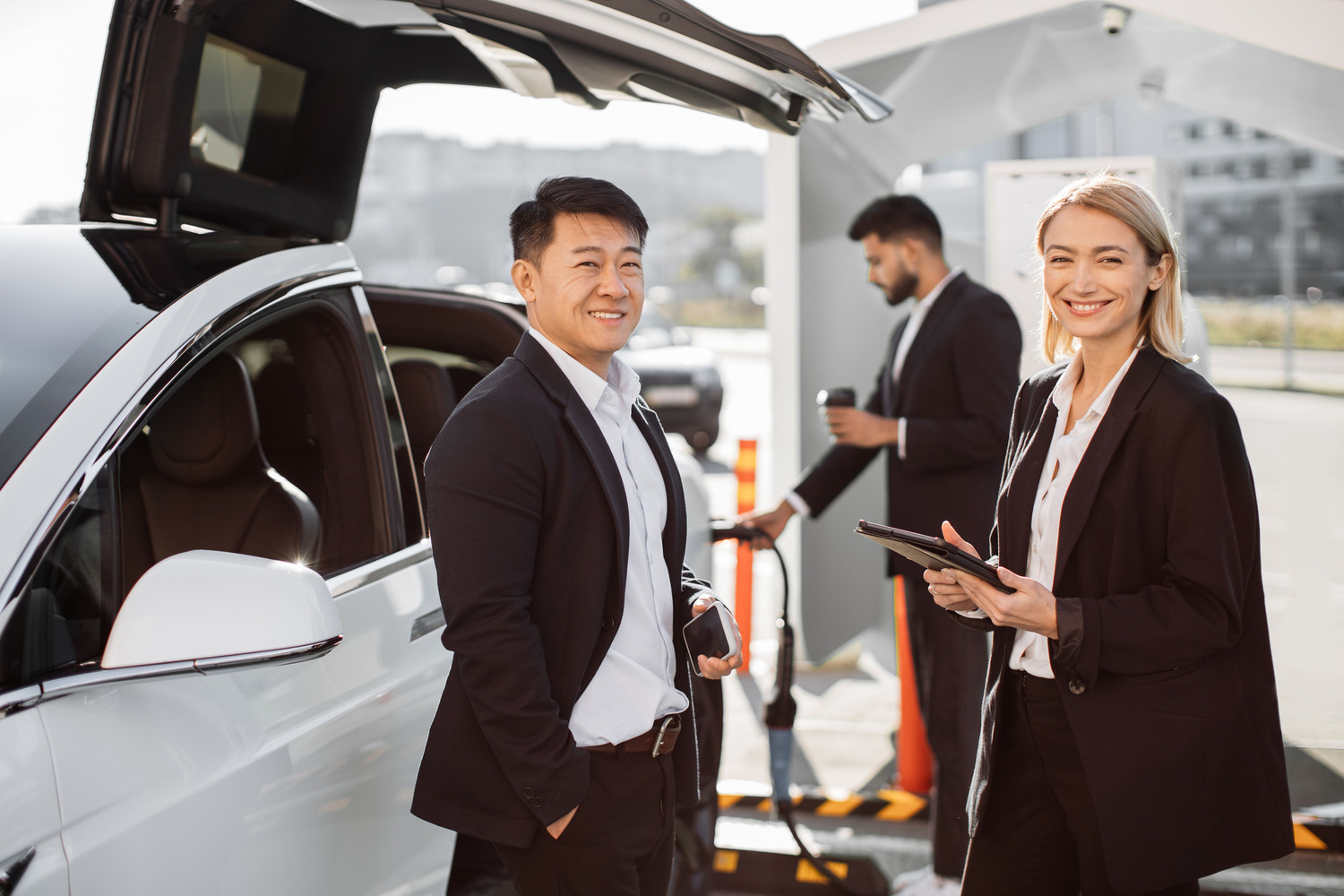Multiracial colleagues standing at station and charging EV